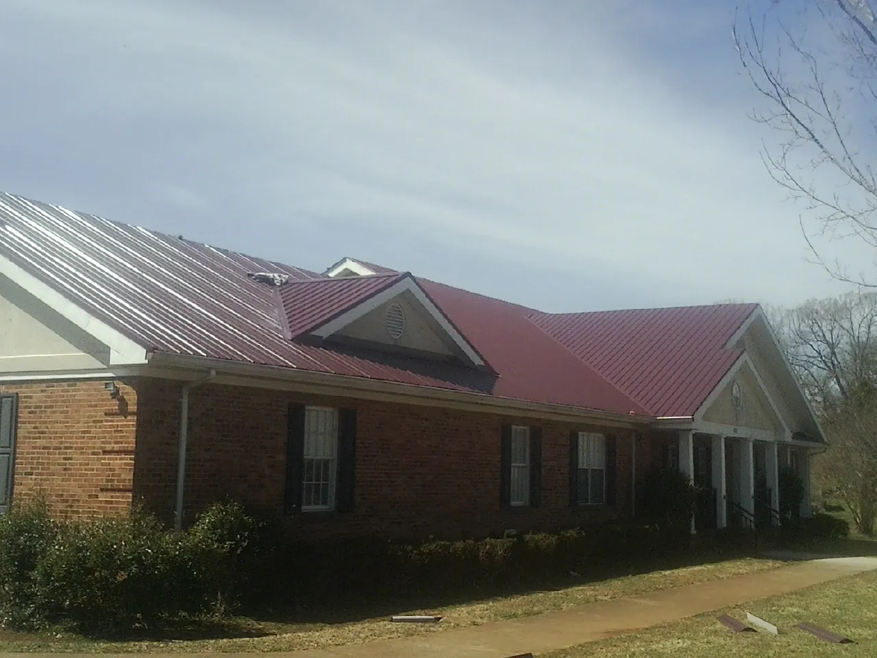 Red metal roof with gabled entries on a long brick building, from a Hail Damage Roof Repair job in Sebring