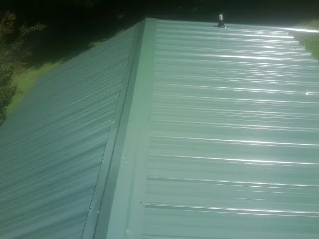 New green metal panels meeting at the ridge of a roof — Flat Roof Repair work by our crew in Sebring